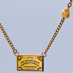 Gold Ouija board necklace on a light grey background